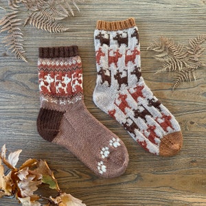 May include: Two pairs of brown and white knitted socks with a reindeer pattern. One pair has a brown background and the other has a beige background.