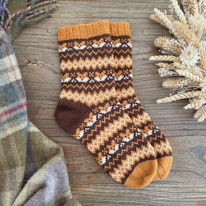 May include: A pair of brown, orange and white patterned knitted socks. The socks have a geometric design and are made from a soft, warm material.