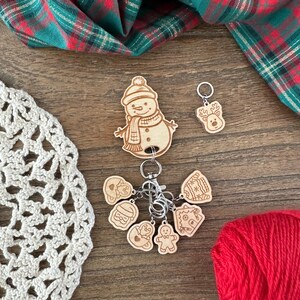 May include: A set of wooden Christmas-themed stitch markers with a snowman, reindeer, gingerbread man, and other designs. The markers are attached to a key ring and are perfect for keeping track of your stitches while crocheting or knitting.