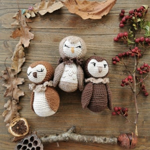 Op de afbeelding: Drie gehaakte uilenspeelgoed in bruin en beige. De uilen hebben hun ogen dicht en zitten op een houten oppervlak.