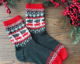 May include: A pair of knitted socks with a festive design. The socks are primarily dark gray with red accents on the toes and cuffs. The pattern includes red cars, white snowflakes, and a red and white zig-zag pattern.