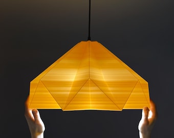 May include: A person holds up a yellow origami-style pendant light with a black cord.