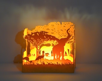 May include: A paper lantern with a silhouette of an elephant and other animals in a jungle setting. The lantern is lit from within, casting a warm glow.