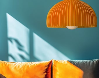 Pode incluir: Uma luminária pendente em forma de cúpula amarelo-brilhante com pregas verticais pende de um fio preto. Abaixo, duas almofadas retangulares laranja repousam sobre uma superfície, iluminadas por luz natural com sombras.