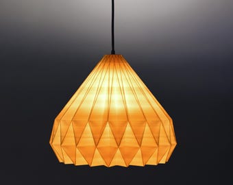 May include: A pendant light fixture featuring a geometric, pleated amber-colored shade with a diamond pattern. The shade is suspended by a thin black cord attached to a matching black circular ceiling canopy, emitting a warm, soft glow.