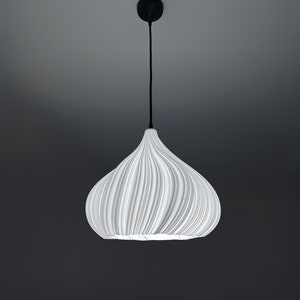 Pode incluir: Uma luminária pendente branca e texturizada com formato bulboso, suspensa por um cabo preto e suporte de teto. A luz tem um design canelado e está sobre um fundo cinza escuro.