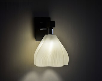 May include: A white, pleated lampshade with a black wall mount. The lamp is turned on and casting a warm glow.