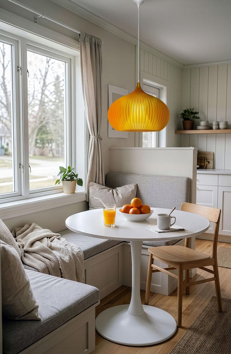 Peut inclure: Une suspension jaune vif avec un abat-jour arrondi et nervur&eacute; est suspendue au-dessus d'une table ronde &agrave; pied central blanc. La table est garnie d'un verre de jus d'orange, d'un bol d'oranges et d'une tasse en c&eacute;ramique, pr&egrave;s d'une banquette grise.