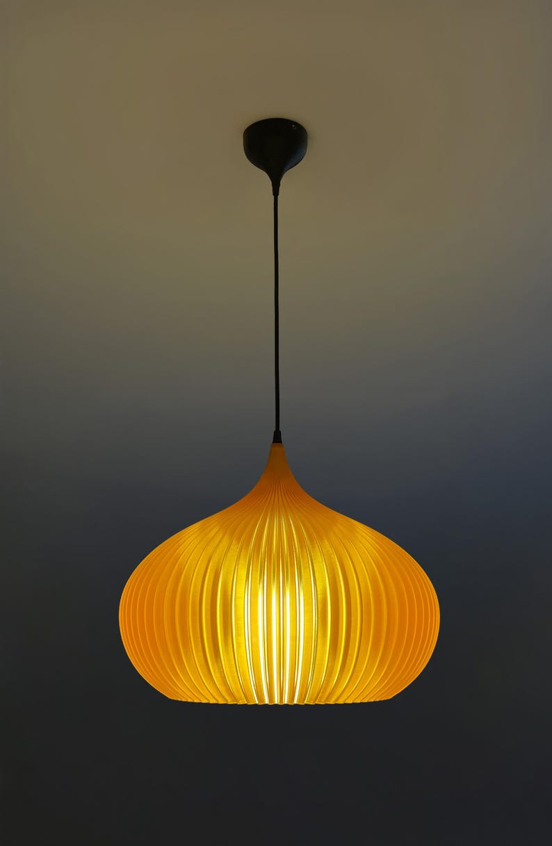 Peut inclure: Une suspension jaune vif avec un abat-jour nervur&eacute; en forme d'oignon. Le luminaire est suspendu par un fin cordon noir attach&eacute; &agrave; une petite rosace de plafond noire. La lumi&egrave;re &eacute;met un &eacute;clat chaud, soulignant les nervures verticales de l'abat-jour.