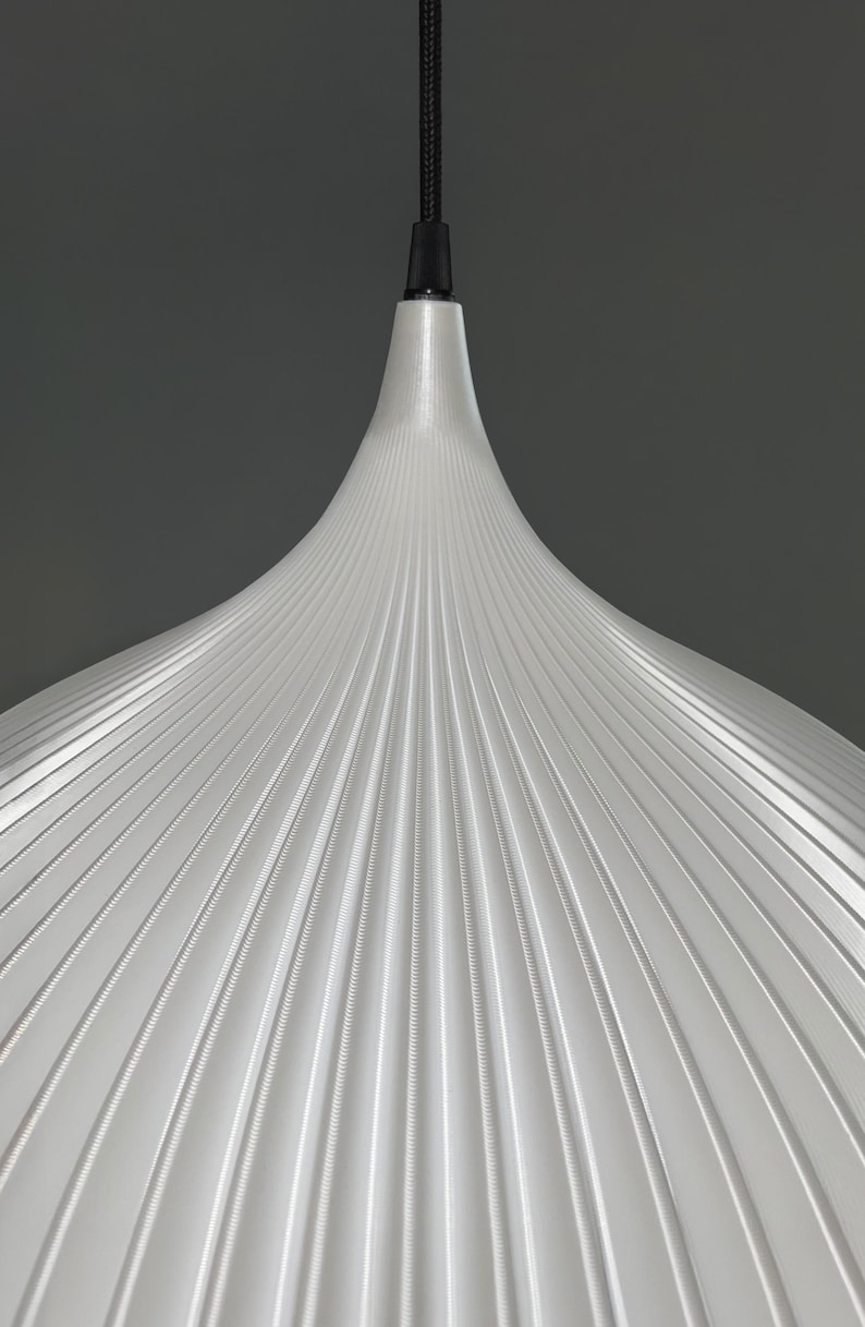 A white pendant light shade with a conical, fluted design featuring vertical ridges radiating from the center. The shade is suspended by a black cord and a black cylindrical fixture at the top, creating a clean, symmetrical appearance.