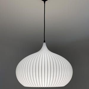 A white pendant light with a rounded, ribbed, onion-shaped shade. The fixture is suspended by a thin black cord attached to a small, circular black ceiling canopy. The shade features vertical ridges that create a textured appearance.