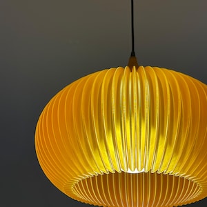 A modern, yellow pendant light with a ribbed, oval shade. The light hangs from a black cord and a wooden fixture. The shade is illuminated from within, creating a warm glow.