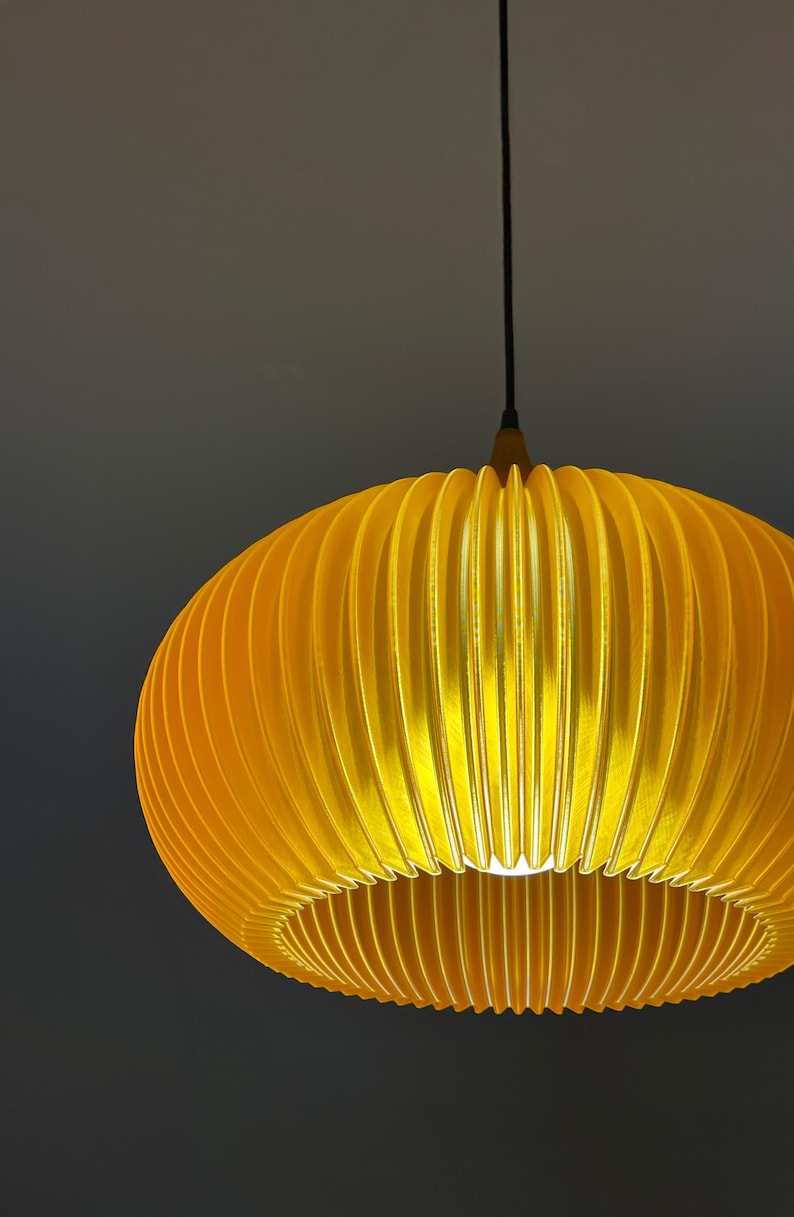 A modern, yellow pendant light with a ribbed, oval shade. The light hangs from a black cord and a wooden fixture. The shade is illuminated from within, creating a warm glow.