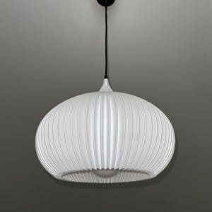 A white pendant light fixture with a rounded, ribbed, and pleated shade. The lamp is suspended by a thin black cord attached to a small, circular black ceiling canopy. A single light bulb is visible inside the bottom opening.