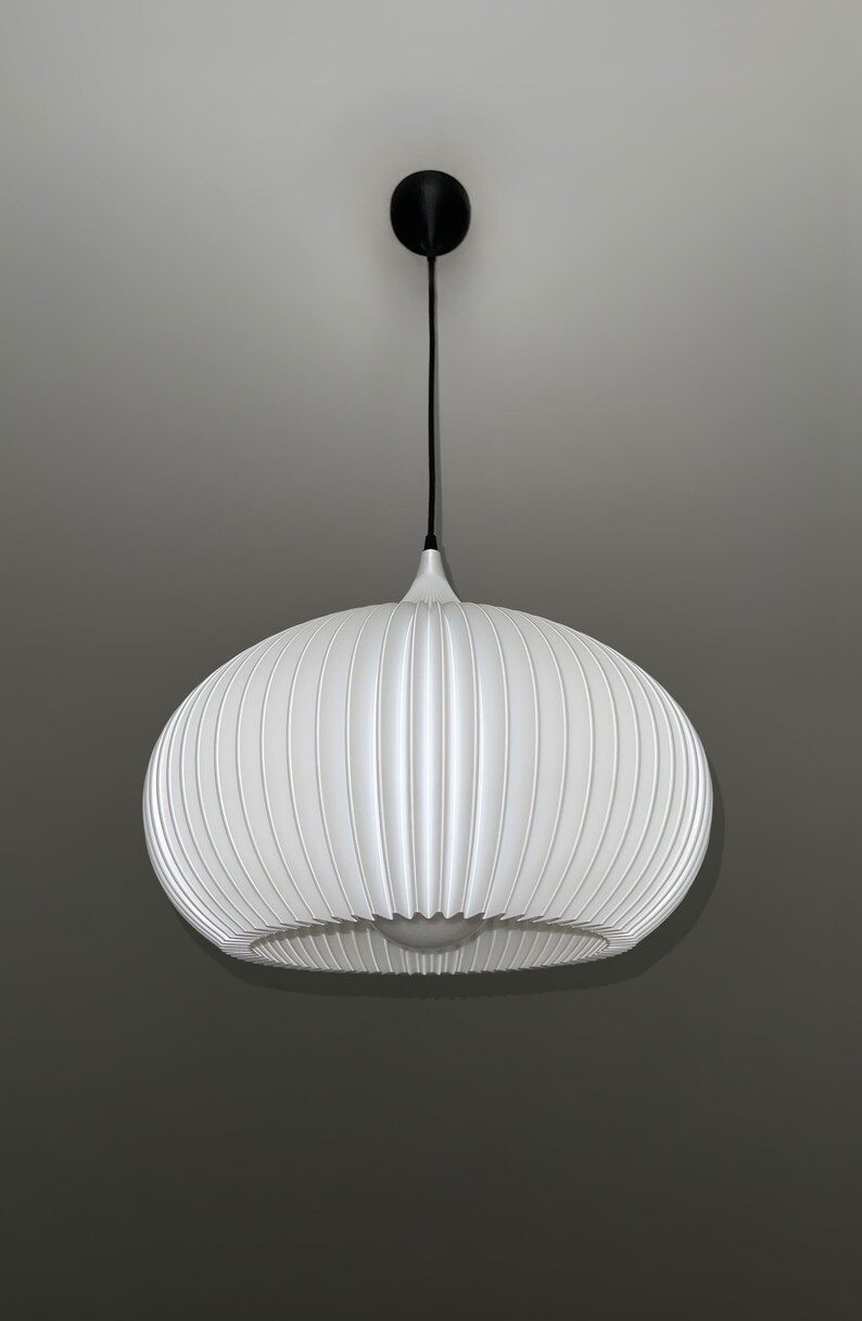 A white pendant light fixture with a rounded, ribbed, and pleated shade. The lamp is suspended by a thin black cord attached to a small, circular black ceiling canopy. A single light bulb is visible inside the bottom opening.