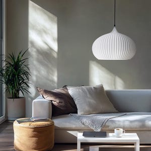 A white pendant light with a ribbed, rounded shade suspended by a thin black cord. The fixture features a smooth, matte finish and a tapered top, providing a clean, uniform appearance that hangs centrally above a seating area.