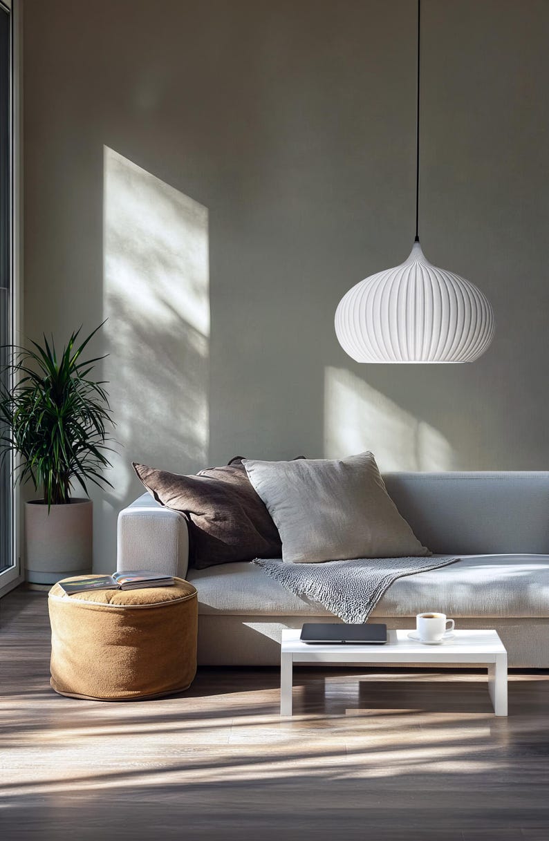 A white pendant light with a ribbed, rounded shade suspended by a thin black cord. The fixture features a smooth, matte finish and a tapered top, providing a clean, uniform appearance that hangs centrally above a seating area.