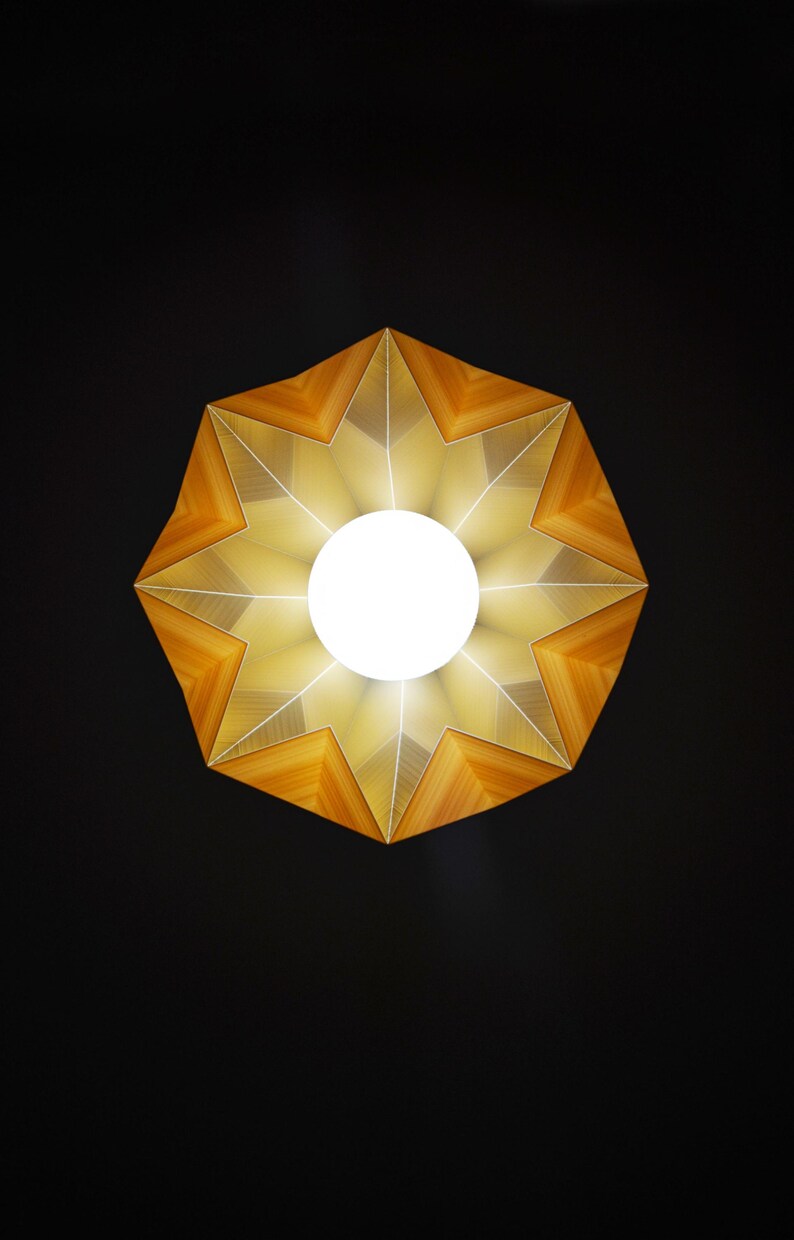 May include: A star-shaped light fixture with a wooden frame and a white light bulb in the center. The light fixture is illuminated, casting a warm glow.
