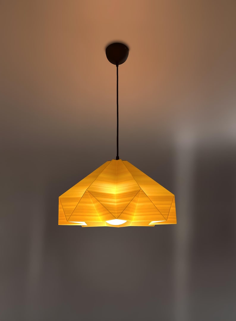 May include: A modern, geometric pendant light fixture with a yellow wood-like shade. The shade is made up of multiple triangular panels, creating a unique and stylish design.