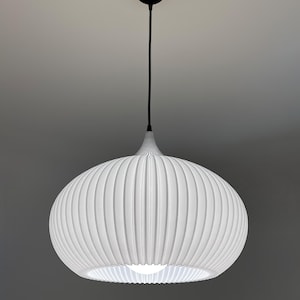 A white pendant light fixture with a rounded, ribbed, and pleated shade. The lamp hangs from a black cord attached to a circular black ceiling canopy. A single bright light bulb is visible inside the center of the white shade.