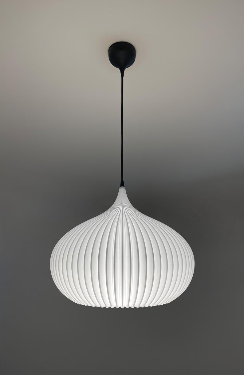 A white pendant light with a rounded, ribbed, and pleated shade. The fixture is suspended by a thin black cord attached to a matching black circular ceiling canopy, creating a clean, symmetrical, and focused lighting element.