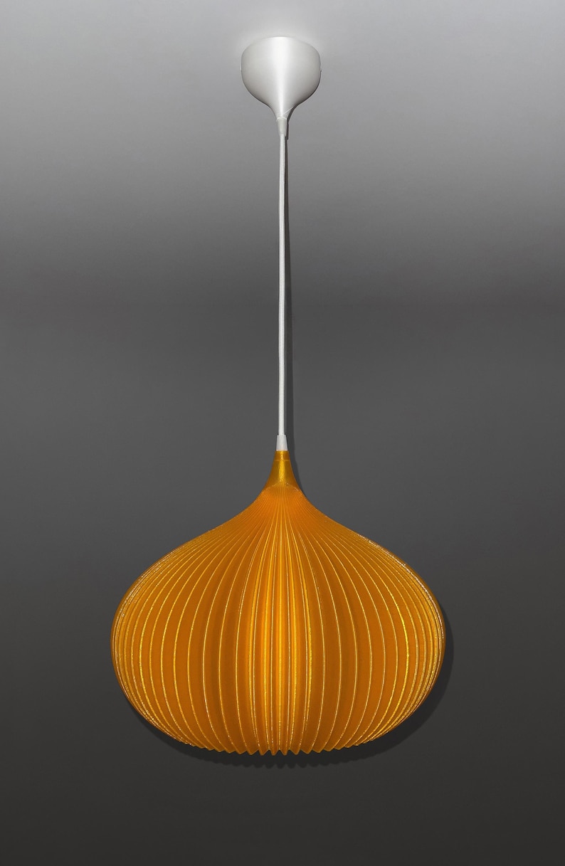 Peut inclure: Une suspension lumineuse dot&eacute;e d'un abat-jour orange vif, nervur&eacute; et en forme d'oignon. La lampe est suspendue par un fin cordon blanc reli&eacute; &agrave; une rosace de plafond blanche assortie. L'abat-jour pr&eacute;sente une texture pliss&eacute;e verticale.