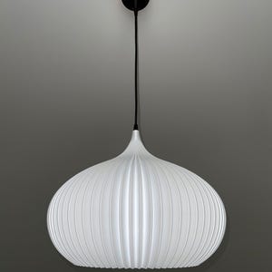 A white pendant light with a rounded, ribbed, pumpkin-like shape. The fixture features a thin black cord extending from the top of the shade to a small, circular black ceiling canopy, creating a clean and simple vertical suspension.