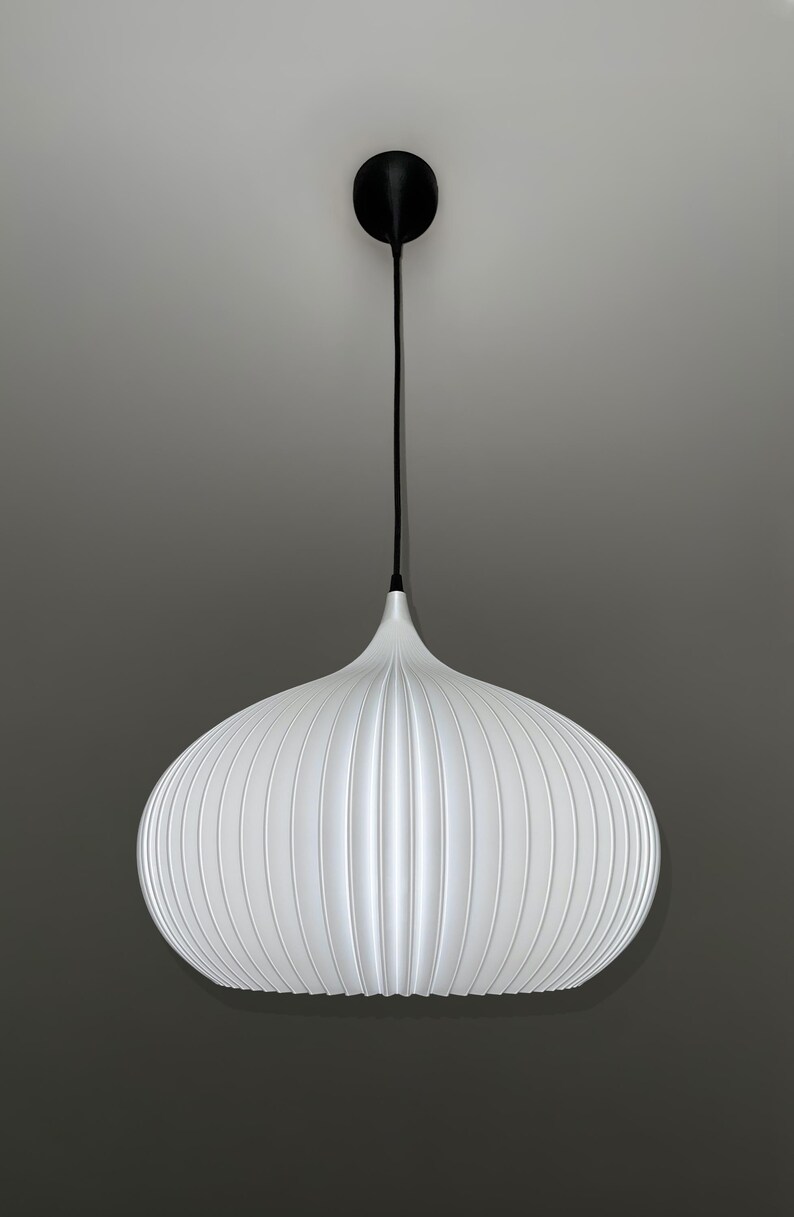 A white pendant light with a rounded, ribbed, pumpkin-like shape. The fixture features a thin black cord extending from the top of the shade to a small, circular black ceiling canopy, creating a clean and simple vertical suspension.