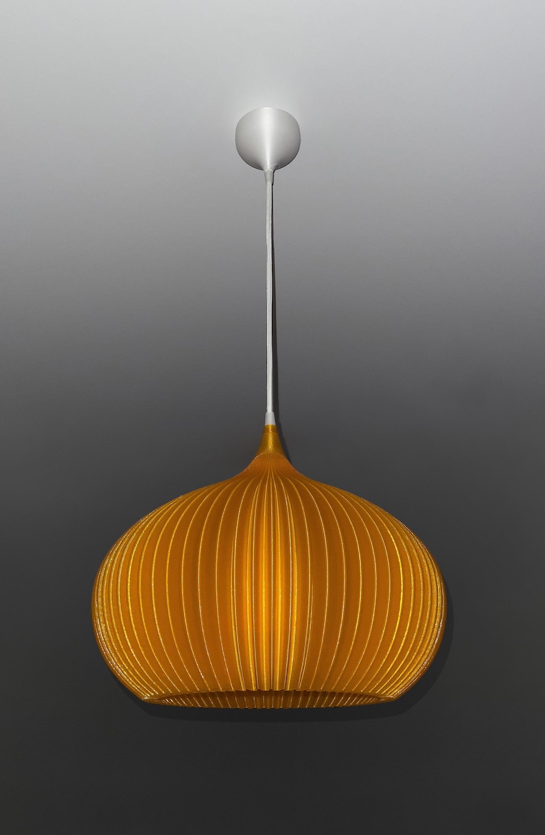 Peut inclure: Une suspension lumineuse jaune dor&eacute; avec une forme arrondie, c&ocirc;tel&eacute;e et semblable &agrave; une citrouille. La lampe pr&eacute;sente une partie sup&eacute;rieure lisse et effil&eacute;e qui se connecte &agrave; un cordon blanc et &agrave; un support de plafond circulaire assorti.