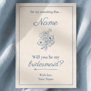 以下が含まれることがあります： 青い文字と花のイラストが入った薄いベージュ色のカード。「For my something blue... Name」と「Will you be my bridesmaid?」と書かれており、名前と挨拶文を入れるスペースがあります。