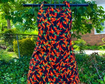 May include: A black apron with a red and green chili pepper pattern. The apron has two pockets on the front.