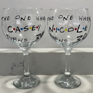 Op de afbeelding: Twee heldere wijnglazen met zwarte letters. De tekst op de glazen luidt "THE ONE WHERE CASEY TURNS 30" en "THE ONE WHERE NICOLE TURNS 30". De namen zijn in de stijl van de tv-serie Friends.