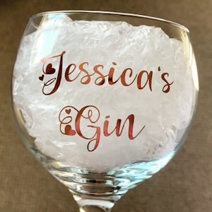 Könnte beinhalten: Ein klares Glas-Gin-Glas mit einem roségoldenen Aufkleber, auf dem "Jessica's Gin" mit zwei kleinen Herzen auf jeder Seite des Textes steht.
