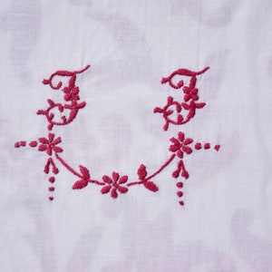 May include: A white fabric with a red embroidered design of two letter "F"s with floral accents.
