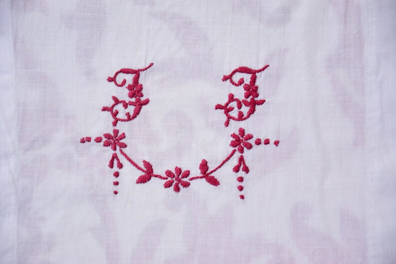 May include: A white fabric with a red embroidered design of two letter "F"s with floral accents.
