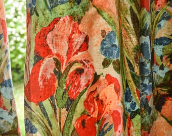 May include: Close-up of a floral patterned curtain with red, orange, blue, and green flowers. The curtain is made of a textured fabric.
