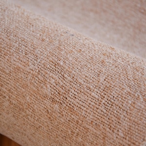 May include: Close-up of a rolled-up beige rug with a woven texture.
