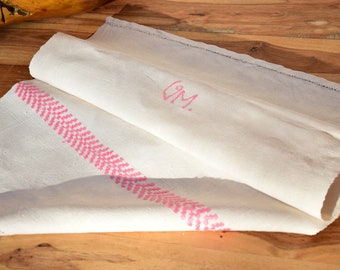 Puede incluir: Un camino de mesa de lino blanco con un borde bordado en rosa y las iniciales "GM" bordadas en rosa.