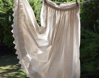May include: A white linen apron with a lace trim hanging on a clothesline. The apron is billowing in the wind.
