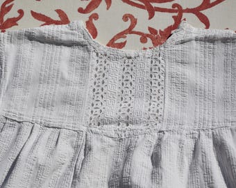 May include: White cotton dress with a lace trim around the neckline. The dress has a gathered skirt and a relaxed fit.