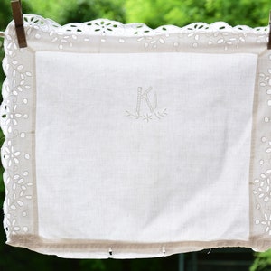 May include: White embroidered linen tea towel with a scalloped edge and the letter "K" embroidered in the centre.
