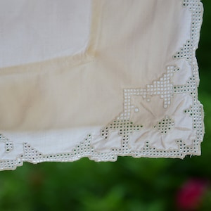 May include: White cotton tablecloth with a delicate embroidered border. The embroidery features a floral design with small, intricate stitches.