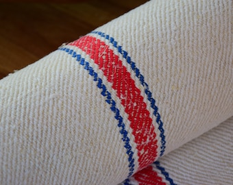 May include: A close-up of a white fabric with red and blue stripes. The fabric is woven with a herringbone pattern.