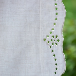 May include: White linen tablecloth with a scalloped edge and a delicate eyelet design. The tablecloth has a subtle texture and a simple, elegant look.
