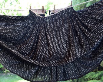 May include: A black skirt with a white, repeating pattern of small shapes, hanging on a clothesline. The skirt is gathered at the waist and flares out, with a ruffled hem. The fabric appears lightweight.