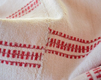 May include: White linen fabric with red woven stripes. The fabric is folded and has a textured surface.