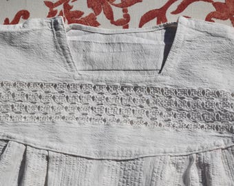 May include: White cotton blouse with a lace trim around the neckline. The blouse has a gathered skirt and a v-neck.