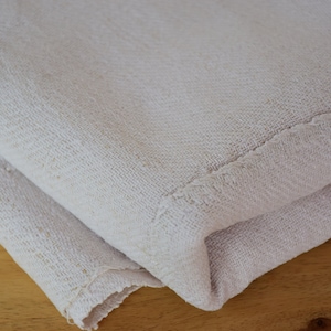 May include: A close-up of a white fabric folded in half. The fabric has a textured surface and a subtle sheen. The fabric is folded over itself, creating a smooth, rounded edge.