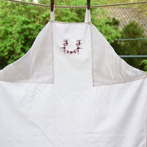 May include: A white linen apron with red embroidered floral details and the letters "JJ" in the center.