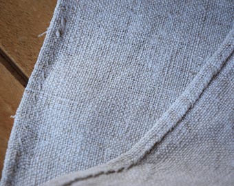 May include: Close-up of a section of beige linen fabric. The fabric has a textured, woven appearance with visible threads and a seam running diagonally across the image. The edges of the fabric are slightly frayed.